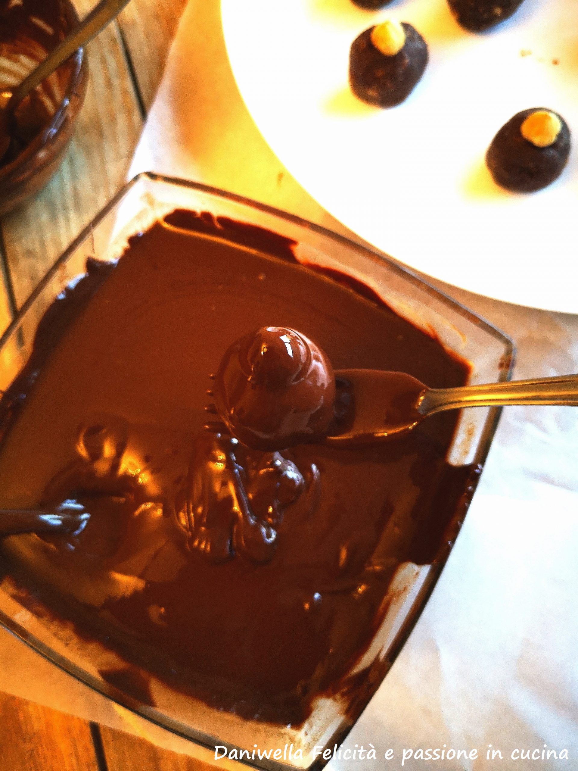 Sciogliete il cioccolato fondente e il burro a bagno Maria,. Mettete in una ciotolina alta e stretta il cioccolato. Poggiate ogni pallina su una forchetta e immergetela nel cioccolato fluido e privo di grumi. Tirate su la forchetta in modo che il cioccolato in eccesso coli, eppoi riponete ogni cioccolatino sulla carta forno.